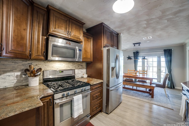 kitchen featuring visible vents, light stone countertops, light wood-type flooring, decorative backsplash, and appliances with stainless steel finishes