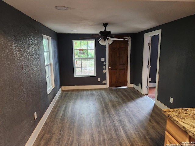 interior space with ceiling fan, dark wood-type flooring, baseboards, and a textured wall