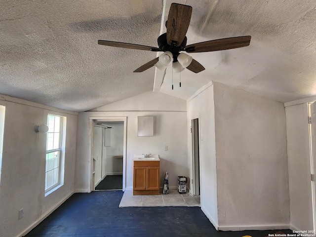 unfurnished bedroom with baseboards, vaulted ceiling, a textured ceiling, a ceiling fan, and a sink