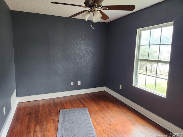 spare room featuring baseboards, wood finished floors, a ceiling fan, and a textured wall