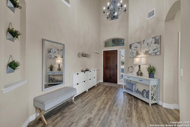 foyer featuring arched walkways, a chandelier, baseboards, and wood finished floors