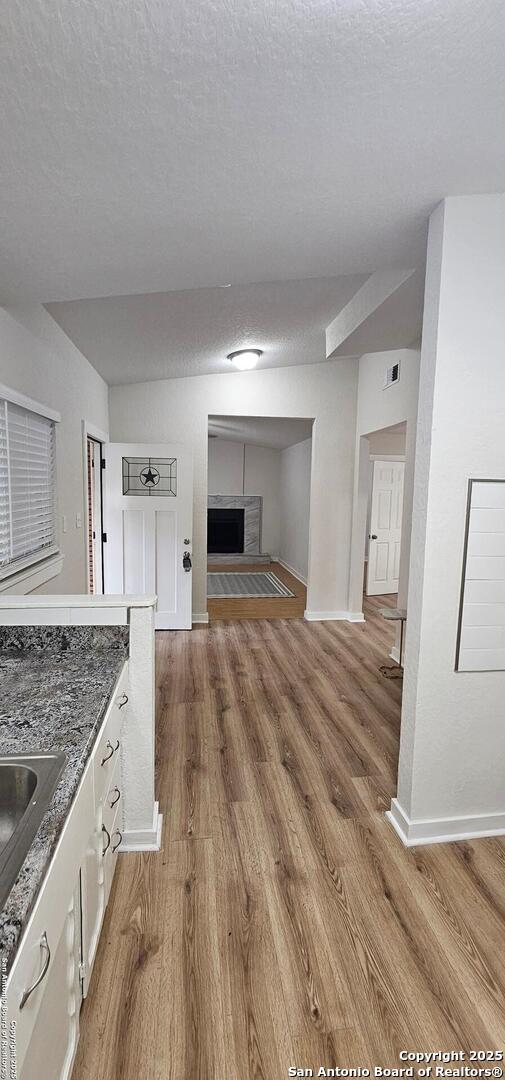 unfurnished living room featuring visible vents, a fireplace with raised hearth, baseboards, light wood-style floors, and a textured ceiling