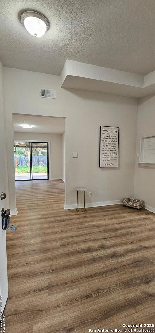 unfurnished room featuring baseboards, wood finished floors, visible vents, and a textured ceiling