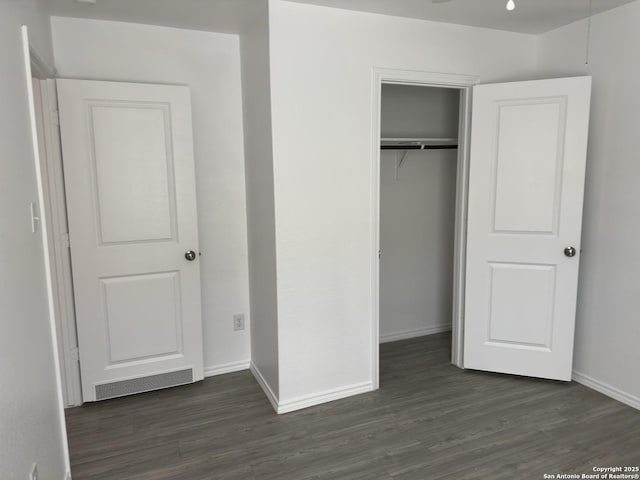 unfurnished bedroom with dark wood-style floors, visible vents, baseboards, and a closet