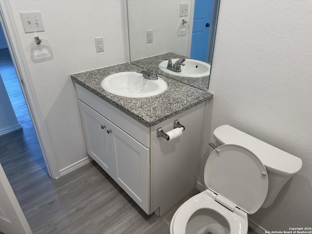 half bath featuring vanity, wood finished floors, baseboards, toilet, and a textured wall