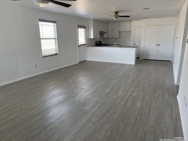 unfurnished living room featuring visible vents, a sink, baseboards, ceiling fan, and dark wood-style flooring