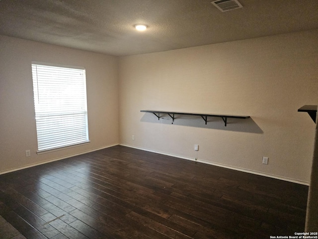 unfurnished room featuring dark wood-style floors, visible vents, a textured ceiling, and baseboards