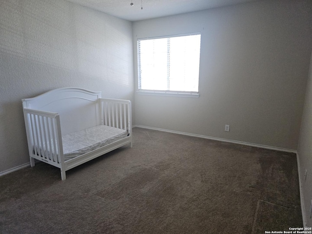 unfurnished bedroom featuring a crib, carpet flooring, and baseboards