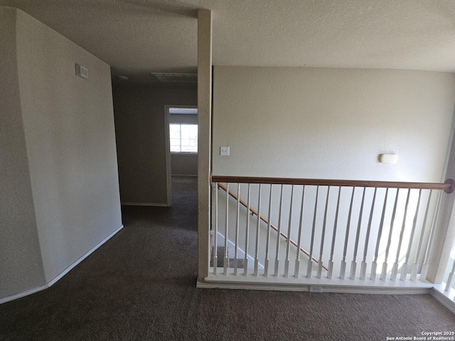 hallway featuring baseboards, carpet floors, and a textured ceiling