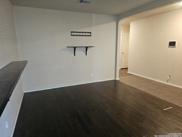 empty room with visible vents, wood finished floors, arched walkways, and baseboards