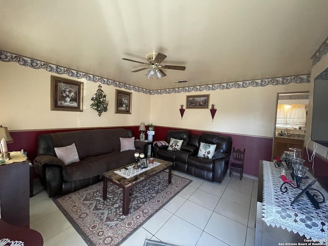 living room with light tile patterned floors, visible vents, wainscoting, and a ceiling fan