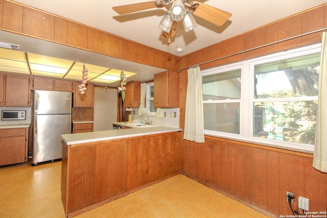 kitchen featuring brown cabinetry, wooden walls, freestanding refrigerator, and a sink