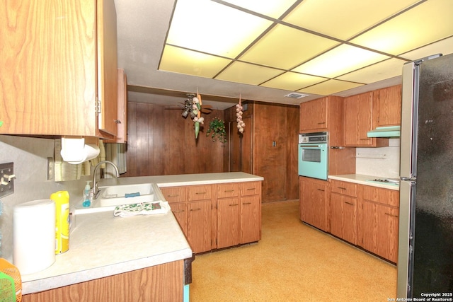 kitchen featuring oven, under cabinet range hood, light countertops, freestanding refrigerator, and a sink