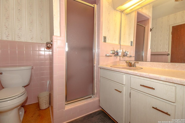 bathroom featuring wallpapered walls, a wainscoted wall, vanity, a stall shower, and tile walls