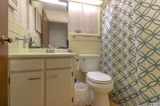 full bath with a wainscoted wall, toilet, tile walls, wallpapered walls, and vanity