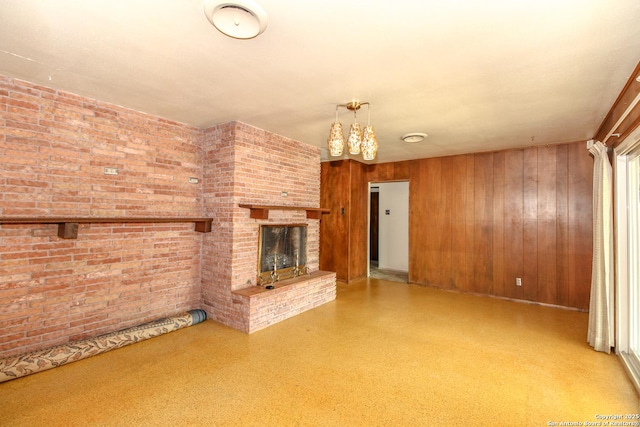 unfurnished living room featuring a brick fireplace, wood walls, and brick wall