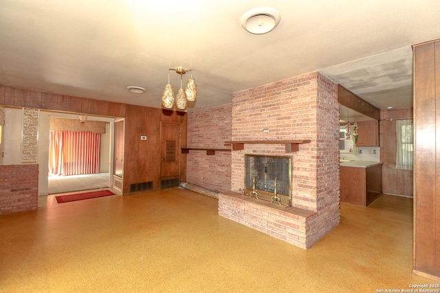 unfurnished living room with a brick fireplace, visible vents, and wood walls