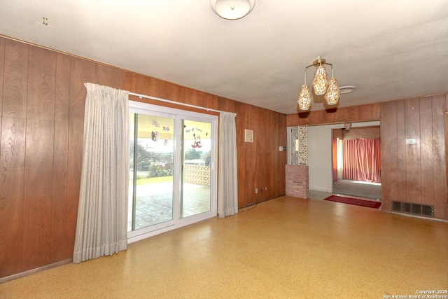 spare room with visible vents, wood walls, and an inviting chandelier