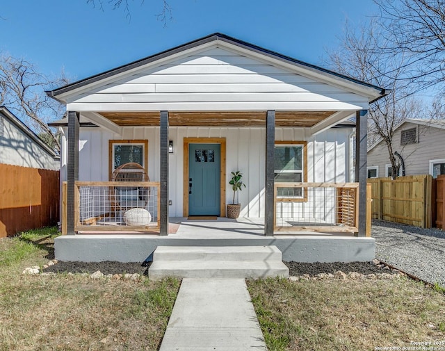 bungalow featuring a porch, board and batten siding, and fence