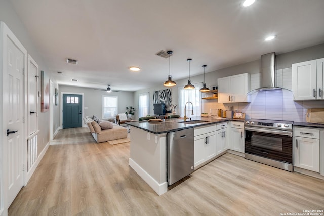 kitchen with dark countertops, visible vents, wall chimney range hood, appliances with stainless steel finishes, and a sink