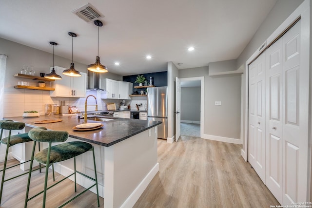 kitchen featuring visible vents, open shelves, freestanding refrigerator, a peninsula, and wall chimney range hood