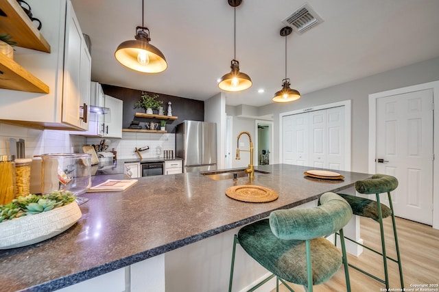 kitchen featuring visible vents, open shelves, a peninsula, freestanding refrigerator, and a sink