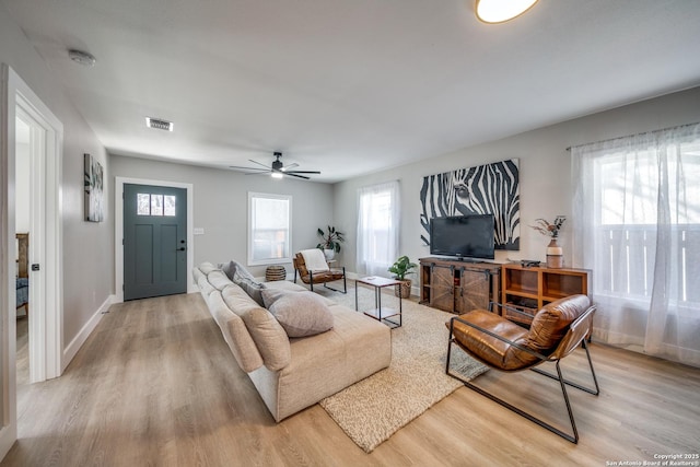 living room with visible vents, light wood-type flooring, and a ceiling fan