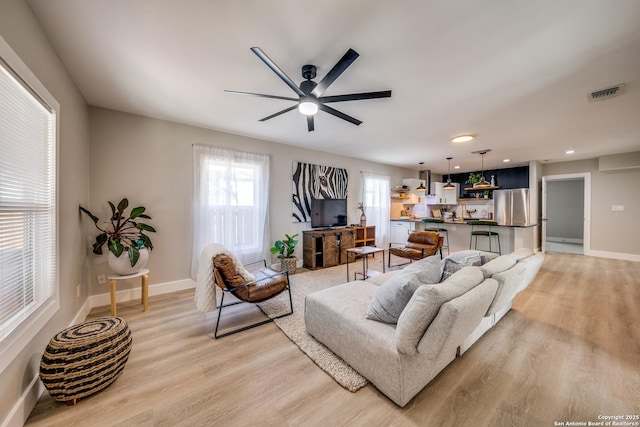 living area with visible vents, baseboards, light wood-type flooring, and a ceiling fan