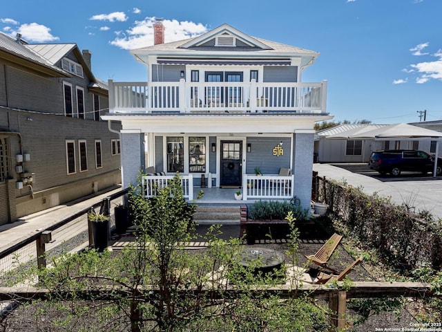 view of front facade with a porch, a balcony, and a chimney