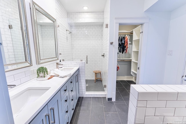 full bath featuring tile patterned flooring, a walk in closet, double vanity, a stall shower, and a sink