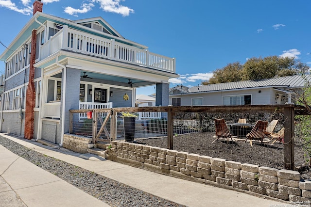 view of front of home with a ceiling fan, a porch, fence, a balcony, and a chimney