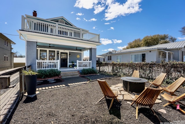 back of property featuring a fire pit, ceiling fan, covered porch, a chimney, and a balcony