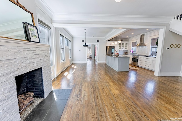 kitchen featuring dark countertops, glass insert cabinets, wall chimney range hood, dark wood finished floors, and white cabinetry