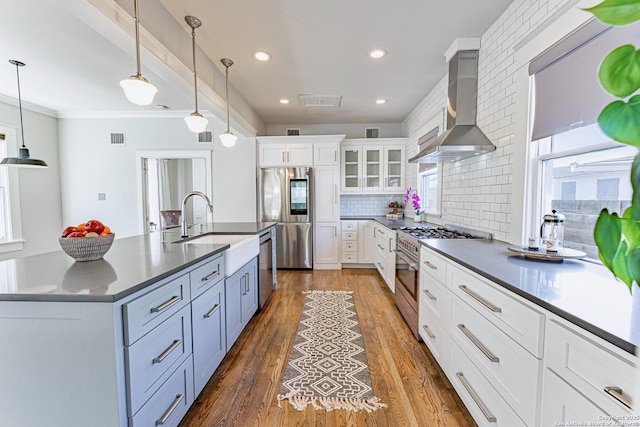 kitchen with dark wood-type flooring, appliances with stainless steel finishes, white cabinetry, dark countertops, and wall chimney exhaust hood