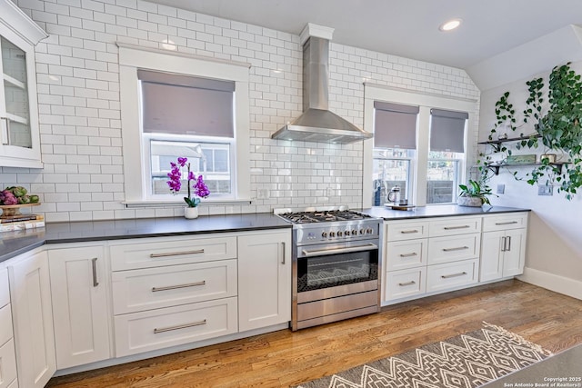 kitchen with light wood-style flooring, stainless steel range, white cabinetry, dark countertops, and wall chimney exhaust hood