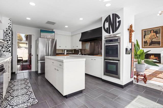 kitchen with a center island, light countertops, white cabinets, stainless steel appliances, and wall chimney exhaust hood