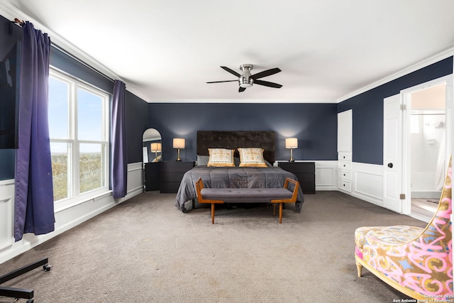 bedroom featuring a wainscoted wall, ceiling fan, ornamental molding, a decorative wall, and carpet flooring