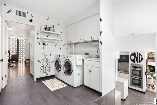 clothes washing area with visible vents, wood tiled floor, washer and clothes dryer, cabinet space, and a sink