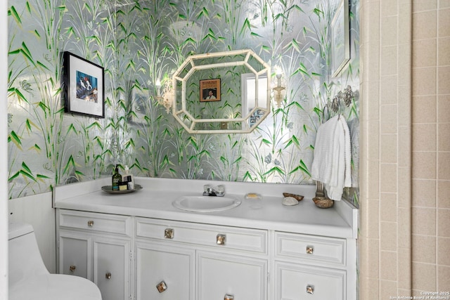 bathroom with toilet, vanity, and wallpapered walls