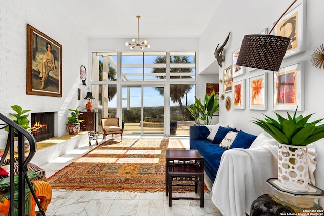 living area featuring a brick fireplace, a notable chandelier, and marble finish floor