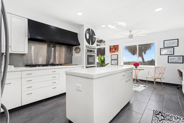 kitchen featuring tasteful backsplash, a kitchen island, ventilation hood, oven, and white cabinets