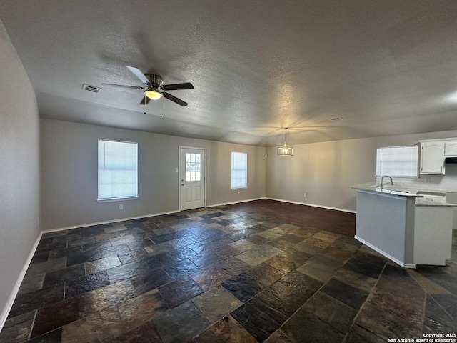 interior space featuring a ceiling fan, baseboards, visible vents, a sink, and stone tile flooring