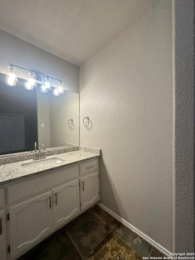 bathroom with a textured ceiling, vanity, baseboards, and a textured wall