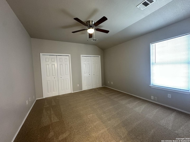 unfurnished bedroom with baseboards, visible vents, carpet floors, vaulted ceiling, and two closets