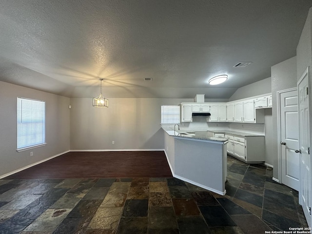 kitchen with visible vents, baseboards, vaulted ceiling, stone tile flooring, and white cabinetry