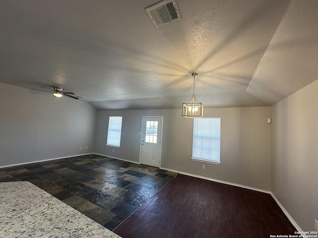 interior space featuring visible vents, baseboards, vaulted ceiling, and ceiling fan with notable chandelier