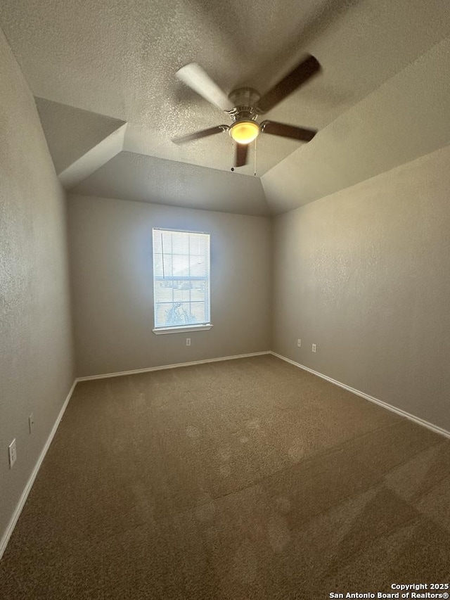 unfurnished room with lofted ceiling, a textured ceiling, dark carpet, baseboards, and ceiling fan