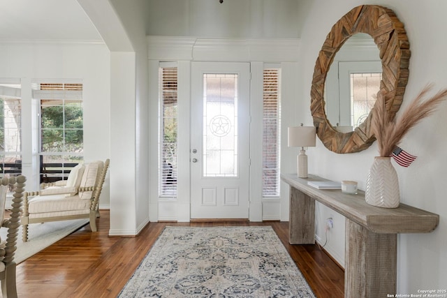 foyer entrance with arched walkways, ornamental molding, baseboards, and wood finished floors