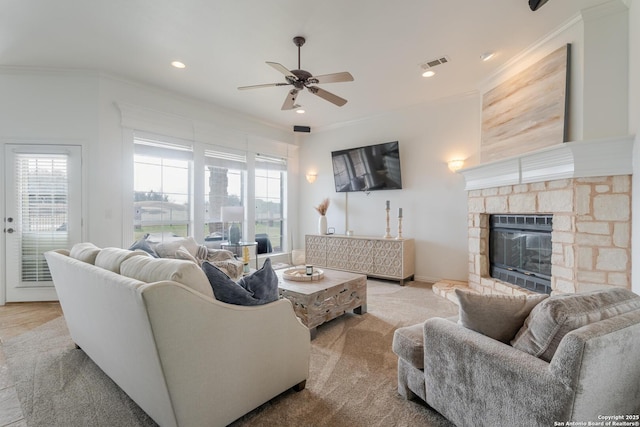 living room featuring visible vents, a stone fireplace, crown molding, and a ceiling fan