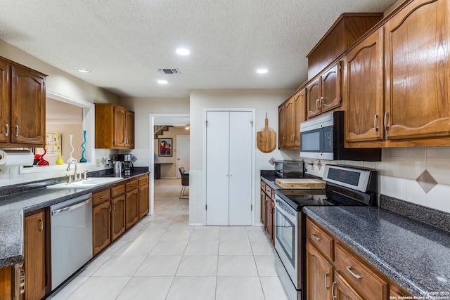 kitchen featuring backsplash, light tile patterned floors, brown cabinets, stainless steel appliances, and a sink